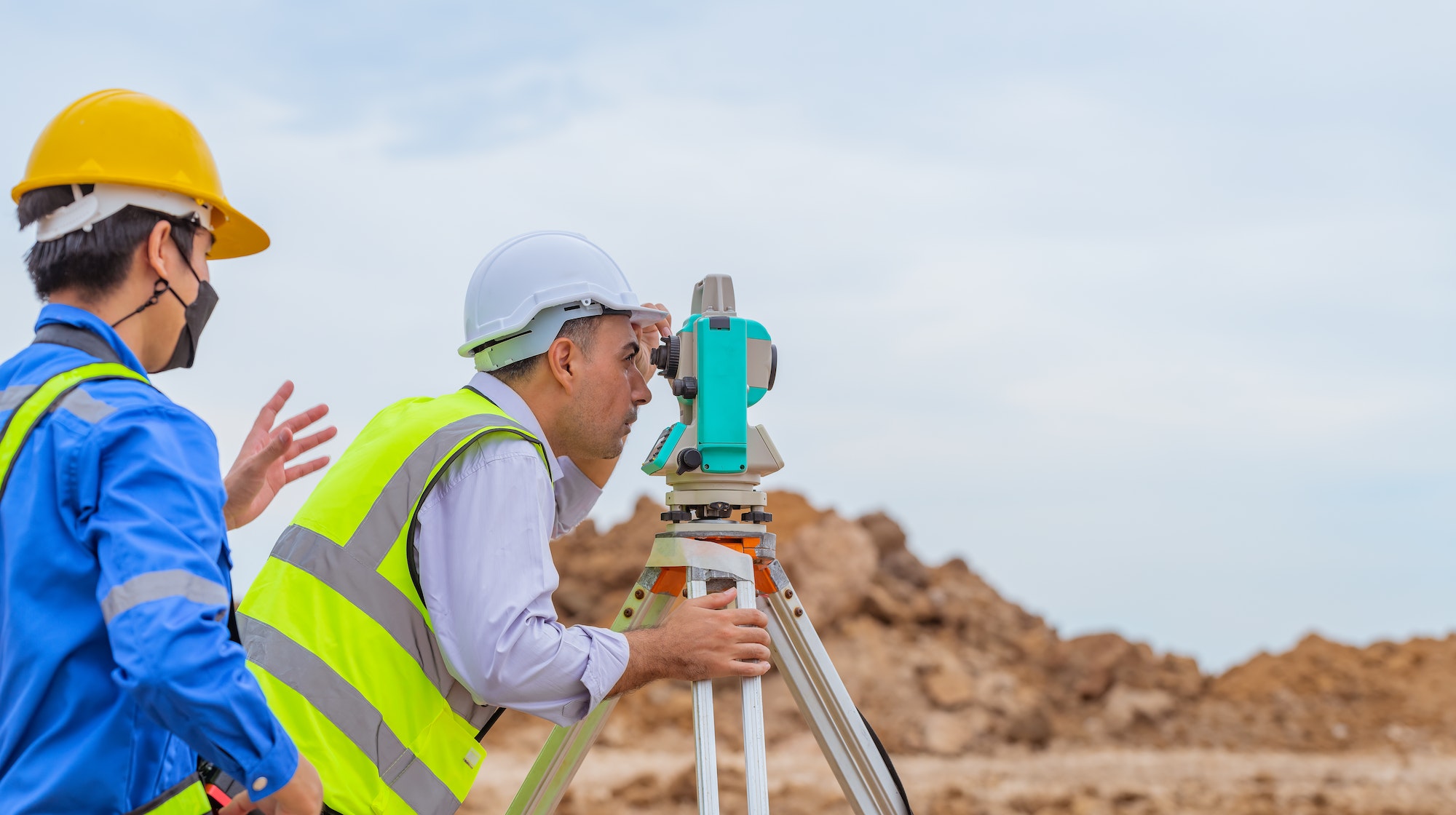 Surveyor engineers wearing safety uniform ,helmet and radio communication with equipment theodolite